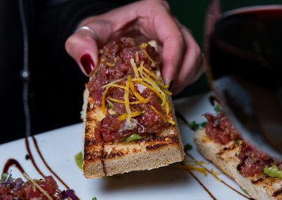 person holding bread with beef tartare over a white plate