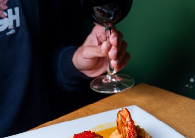 person holding glass of wine with seared scallops and jumbo shrimp on their plate